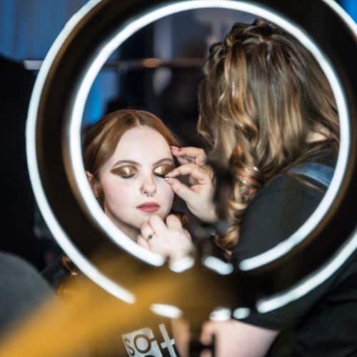 Makeup artist applying eyeshadow to a woman in a salon through a ring light.