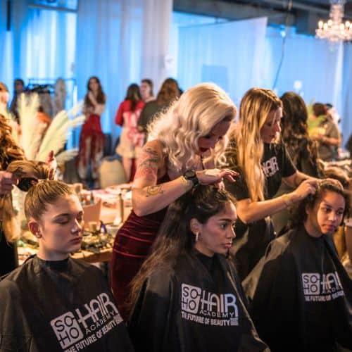 Hair stylists working on models' hair at a beauty school event.