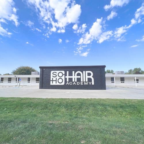Single-story building with "soho hair academy and cosmetology school" sign under a clear sky.