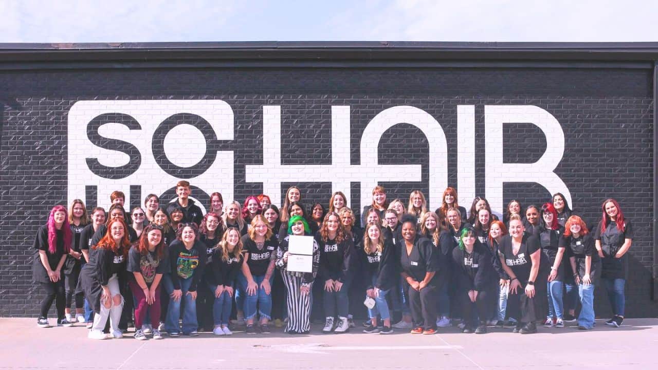 A group of individuals posing for a photo in front of a wall with the word "choir" written on it at an Omaha cosmetology school.