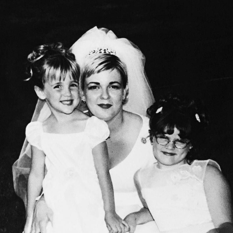 A bride posing with two young girls in formal dresses, all showcasing hairstyles perfected at a cosmetology school, presumably at a wedding in Omaha.