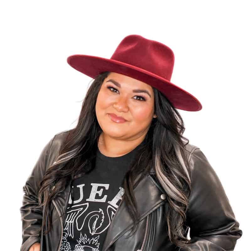A woman wearing a red hat and a black leather jacket smiles at the camera after attending an Omaha cosmetology school.