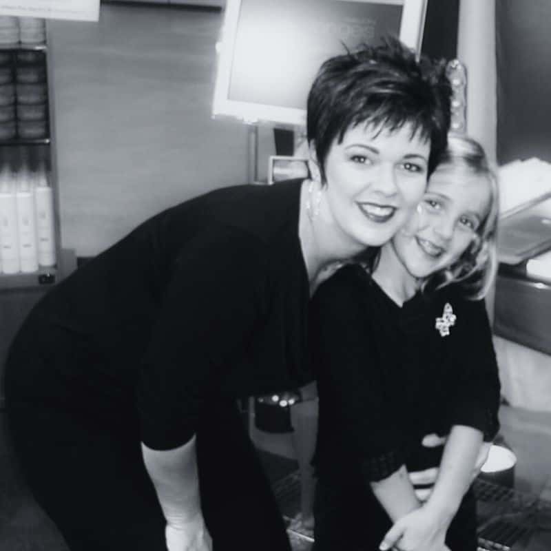A woman and a young girl smiling and embracing in a beauty salon, captured in a black and white photo.