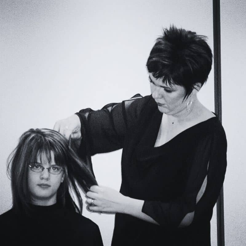 A cosmetology school graduate cutting a client's hair in a salon.