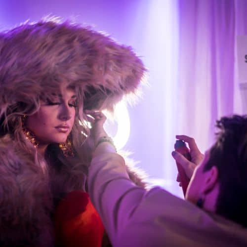 Person in a fur hat receiving a makeup touch-up at a salon before an event.