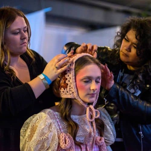 Two makeup artists styling a model's hair and adjusting her headpiece backstage at an Omaha beauty hair salon.