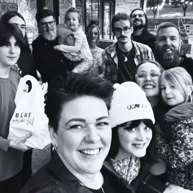 A group of people of various ages smiling for a selfie outside an Omaha salon, with some holding shopping bags.