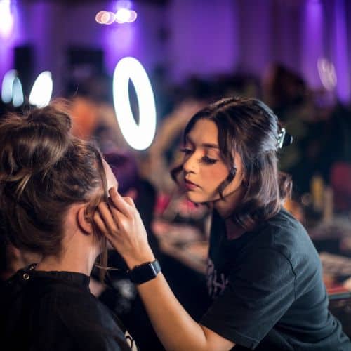 Makeup artist applying beauty cosmetics to a client backstage.