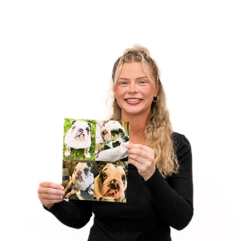 A woman with long blond hair wearing a black sweater smiles and holds up a photo collage of a bulldog on a white background.