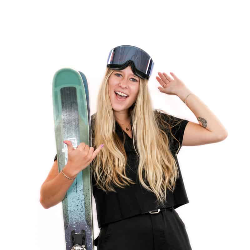 Woman holding a snowboard and wearing a ski goggle, smiling at the camera, her hair styled perfectly from an Omaha salon.