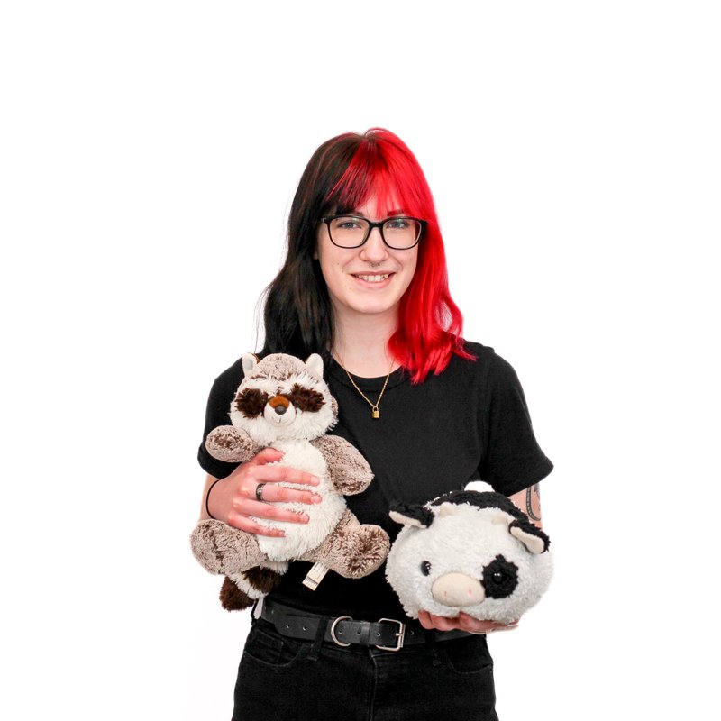 Woman with red hair holding a plush raccoon and a plush cow at school.
