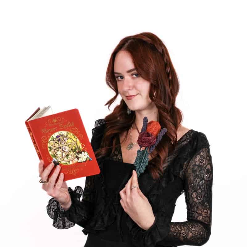 Woman holding a red book with decorative cover, wearing a black lace dress and holding a fabric flower in her beautifully styled hair from a top hair salon.