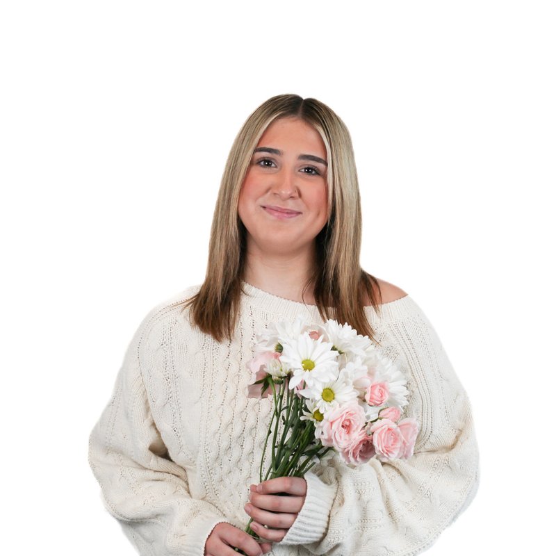 A person with long hair in a cream sweater holding a bouquet of pink and white flowers, standing against a plain white background.