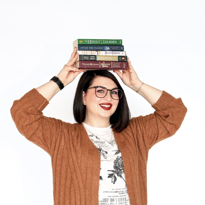 A woman with dark hair and glasses balancing a stack of five books on her head.