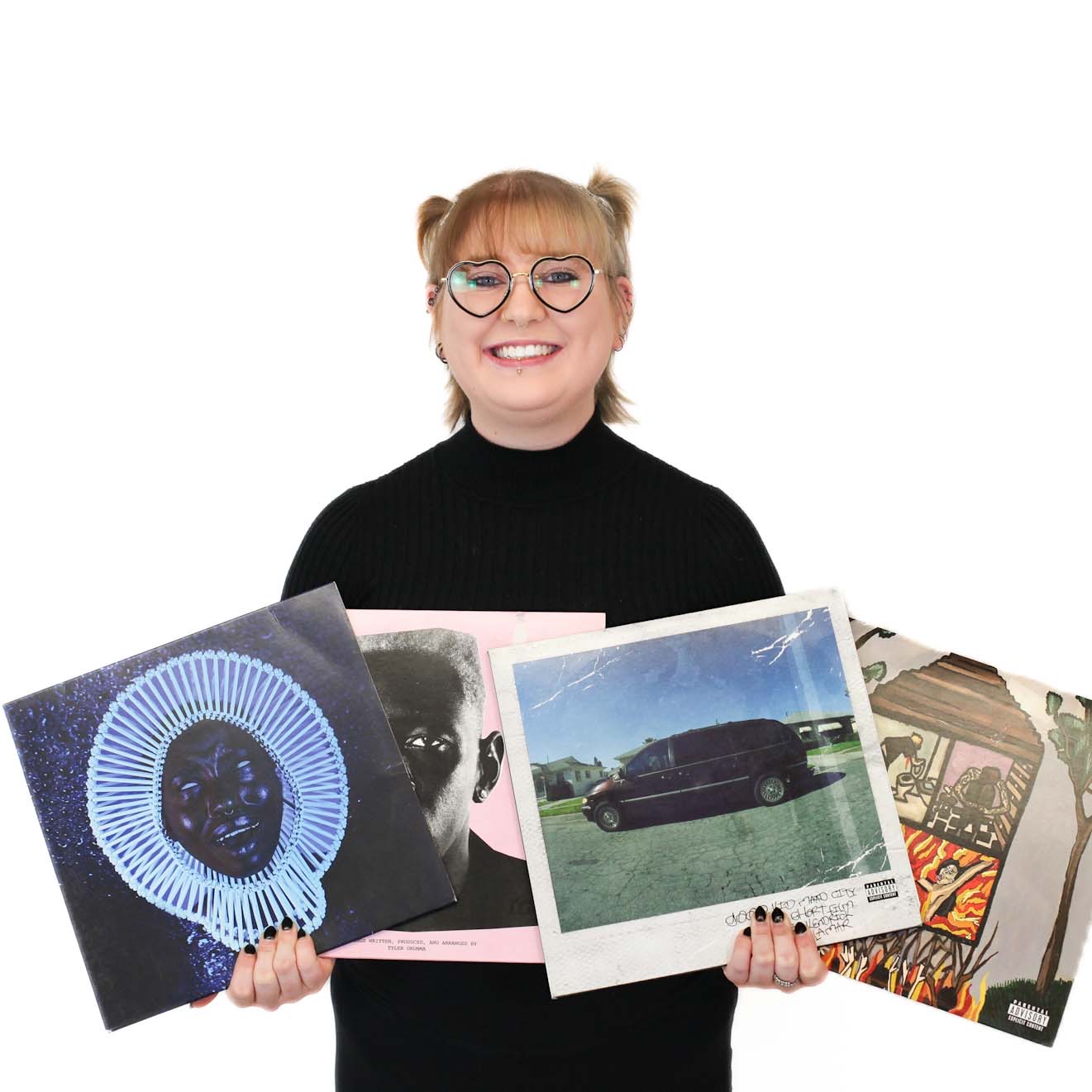 Person smiling and holding four vinyl records, including album covers for Childish Gambino, Kendrick Lamar, Sza, and Tyler, the Creator, against a plain white background.