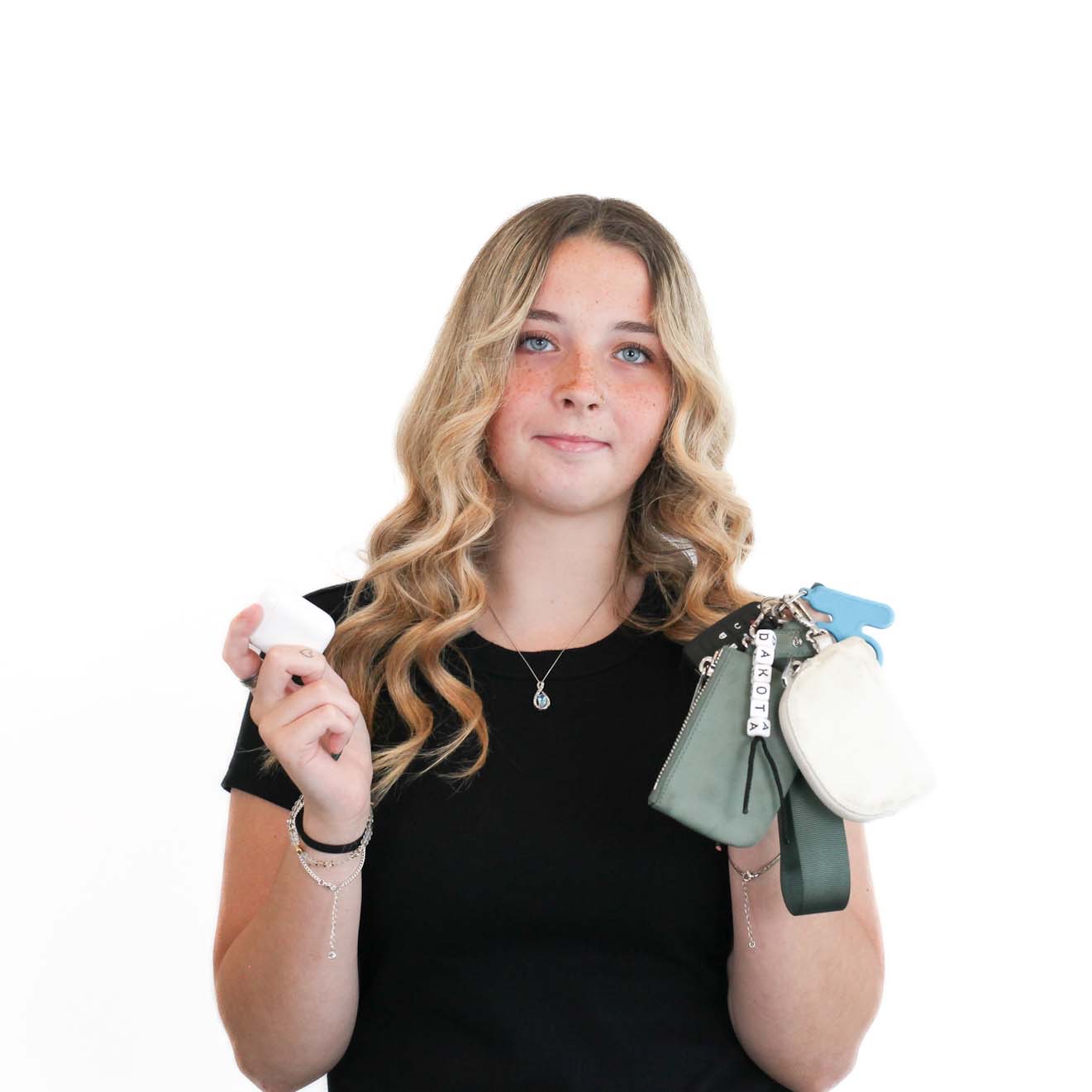 A young woman with wavy blonde hair holds a set of keychains and small pouches in one hand and a small white item in the other, standing against a plain white background.