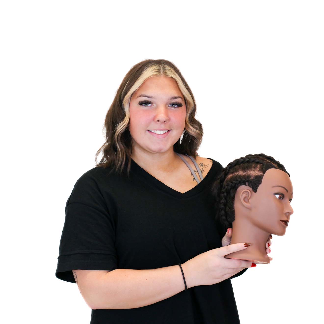 A woman with shoulder-length hair and a black shirt holds a mannequin head with braided hair against a white background.