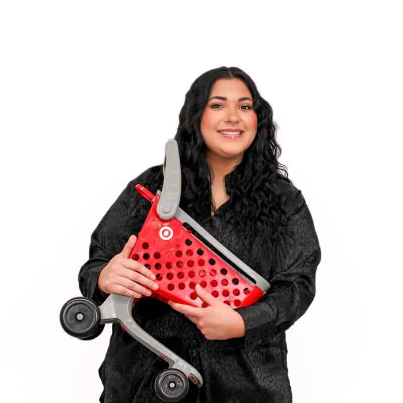 A woman smiling while holding a small red shopping cart with a target logo on a white background.