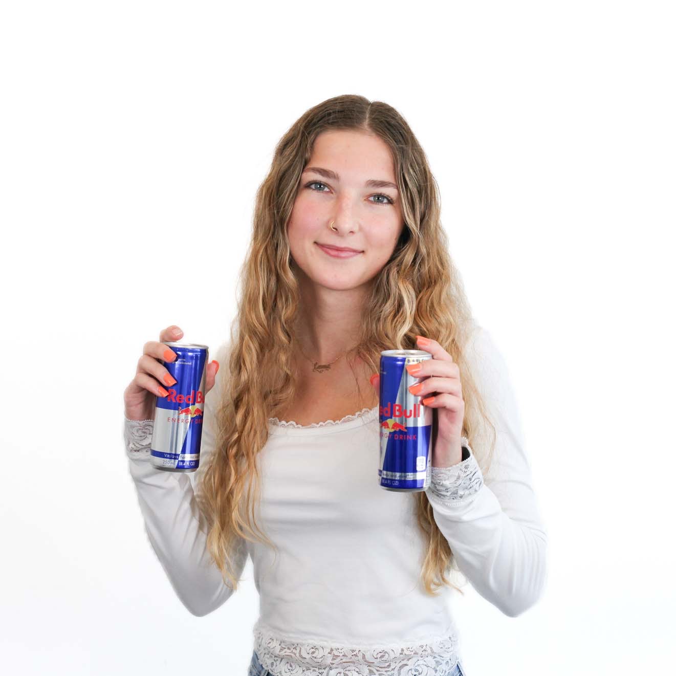 A young woman with long wavy hair holds two cans of Red Bull energy drink, standing against a plain white background.