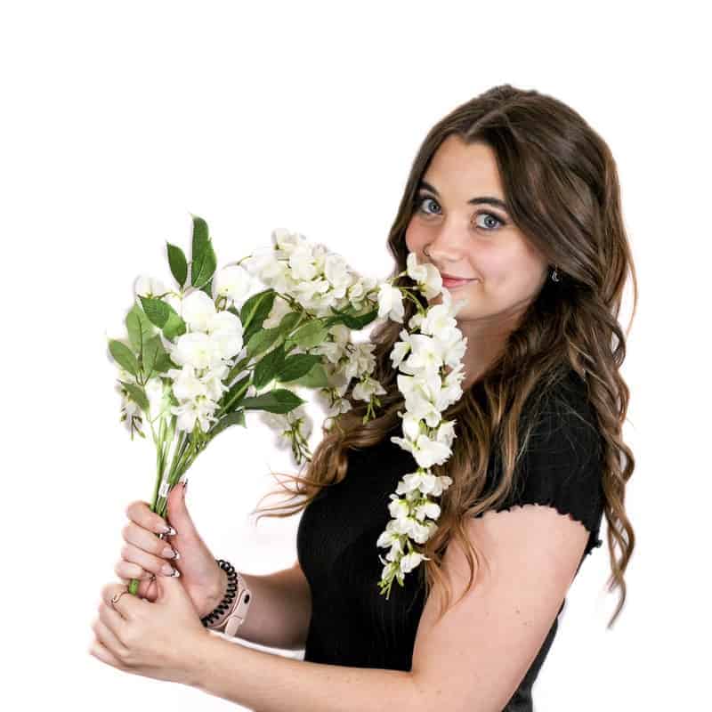 A woman smiling while holding a bouquet of white flowers close to her face, fresh from a beauty salon.