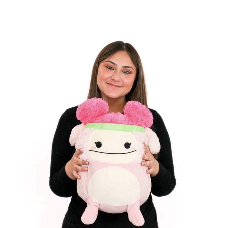 Woman smiling, holding a plush toy with pink details against a white background, obviously thrilled after her visit to the hair salon.