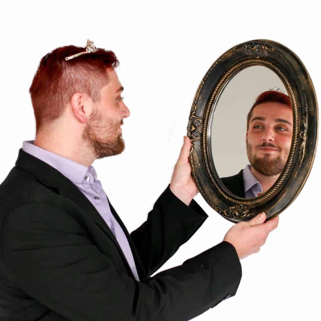 Man holding an ornate mirror at a hair salon and looking at his reflection.