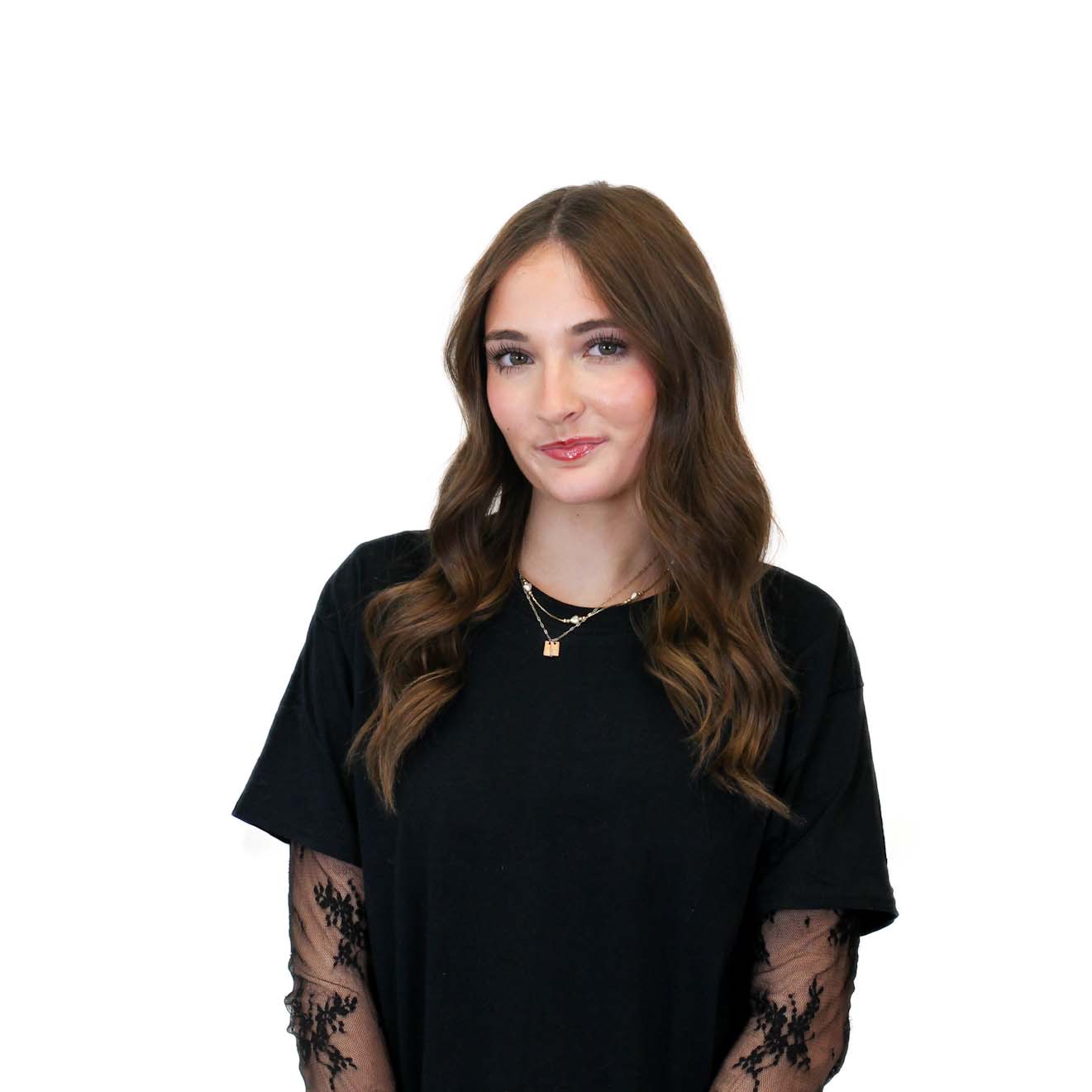 A young woman with long brown hair, wearing a black top with lace sleeves, stands against a plain white background.
