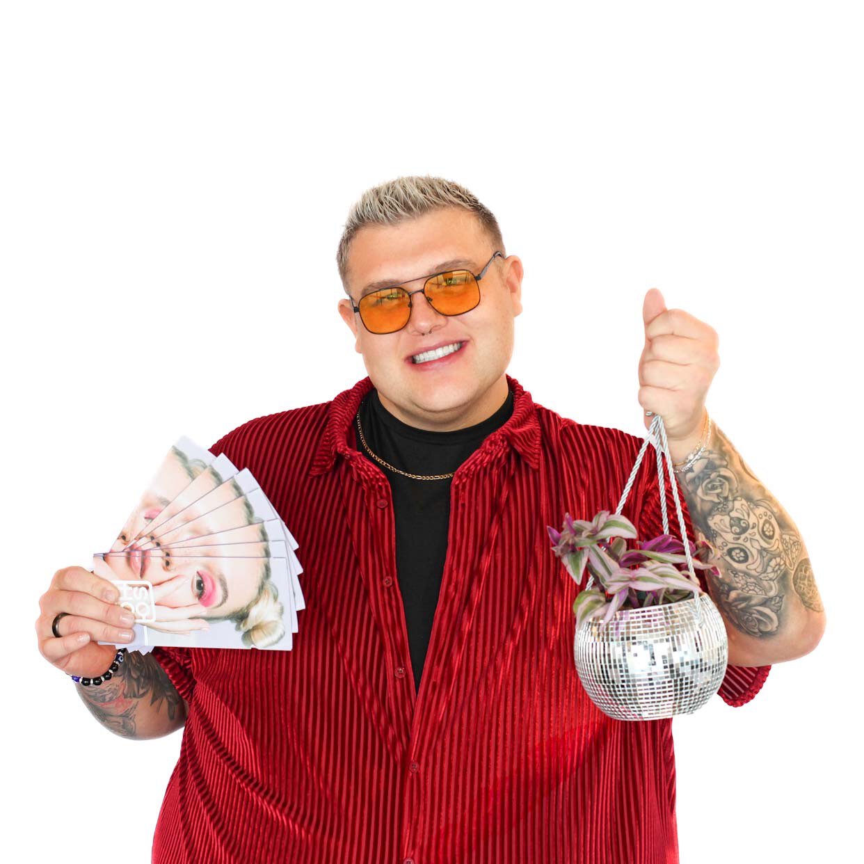 A smiling person in a red shirt holds several face printouts in one hand and a small potted plant in a disco ball planter in the other.