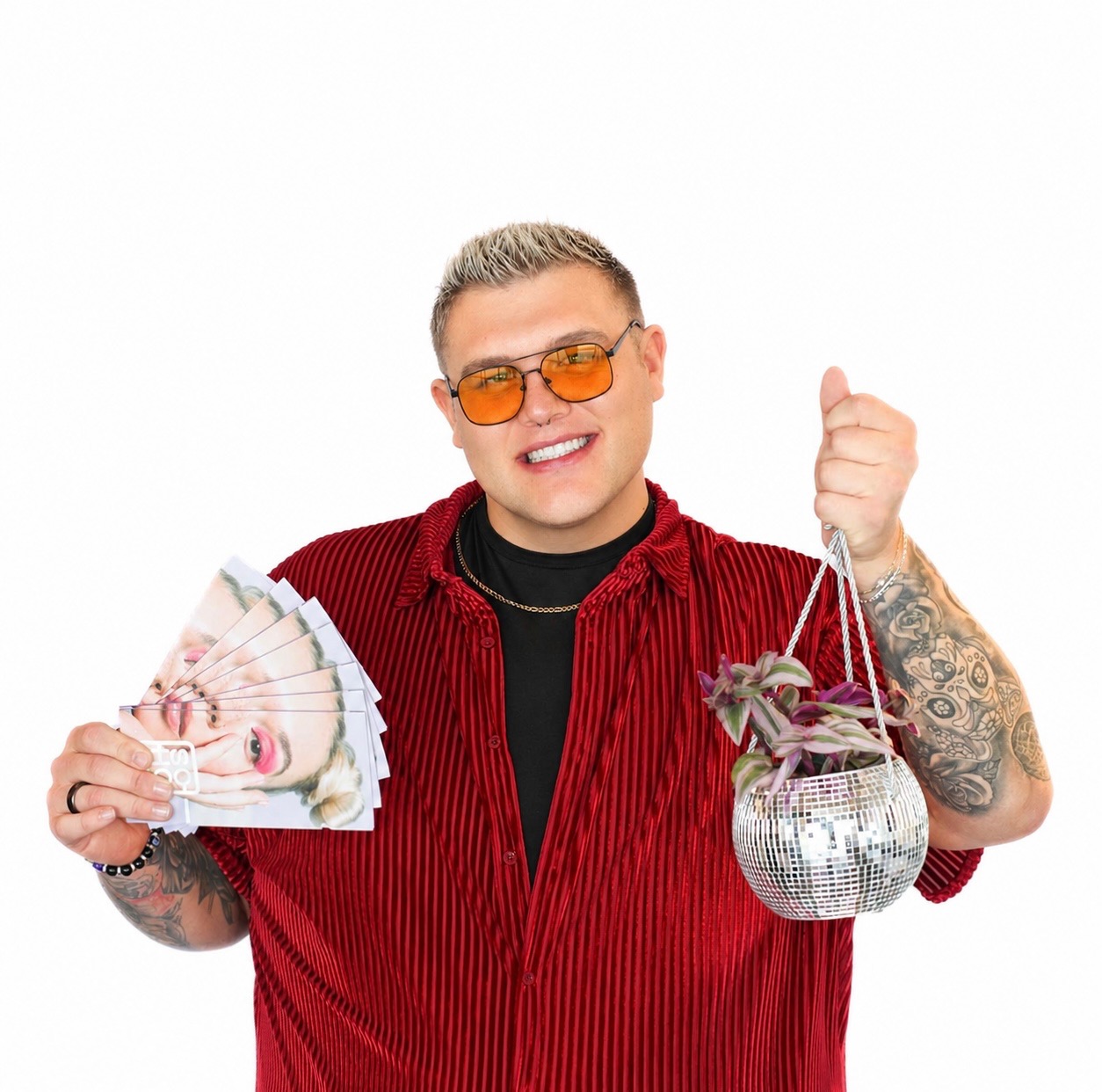 A smiling person in a red shirt holds several face printouts in one hand and a small potted plant in a disco ball planter in the other.
