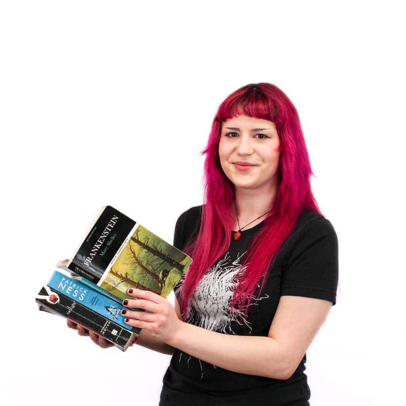 Woman with pink hair from cosmetology school holding a stack of books.