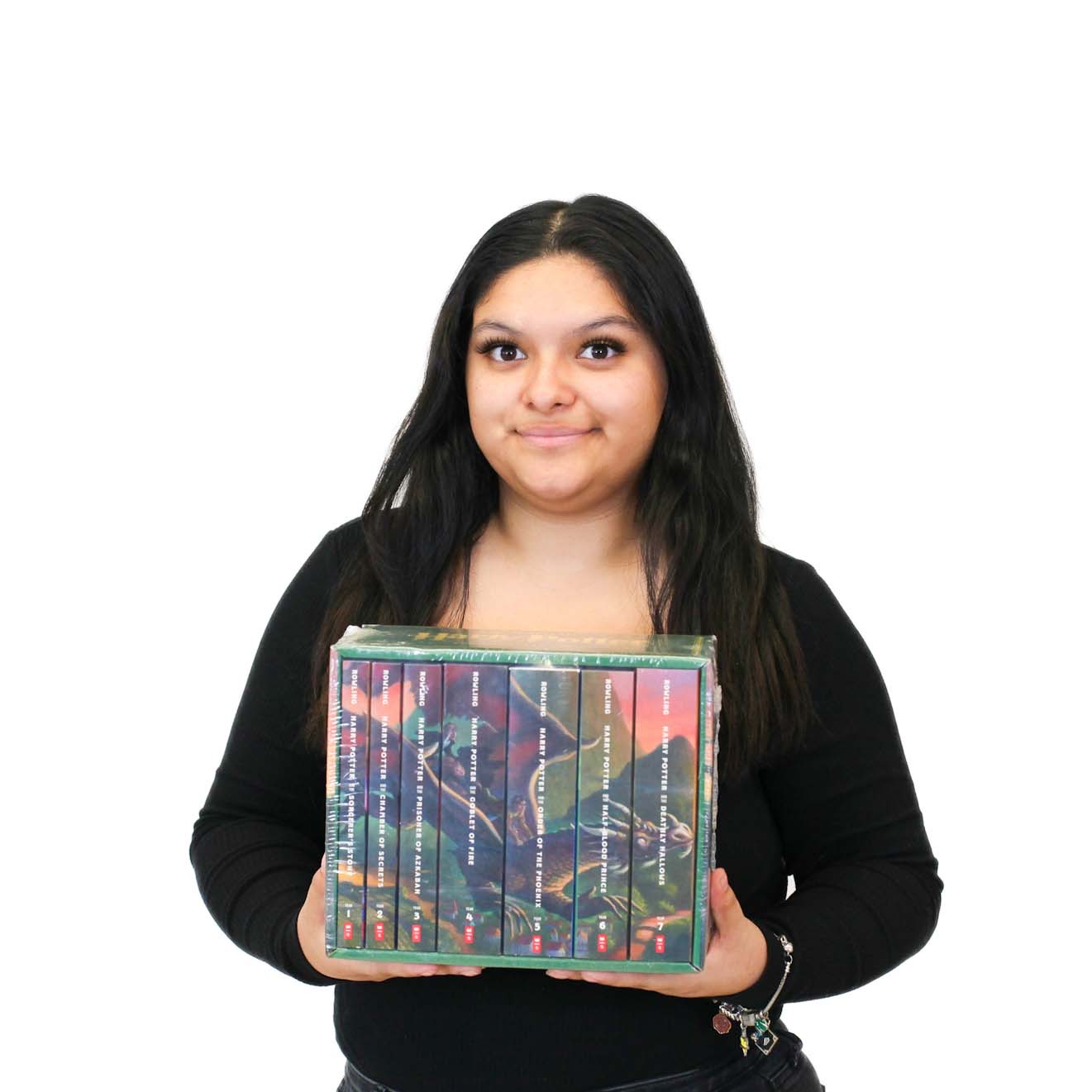 A woman with long dark hair, wearing a black top, holds a box set of books against a plain white background.