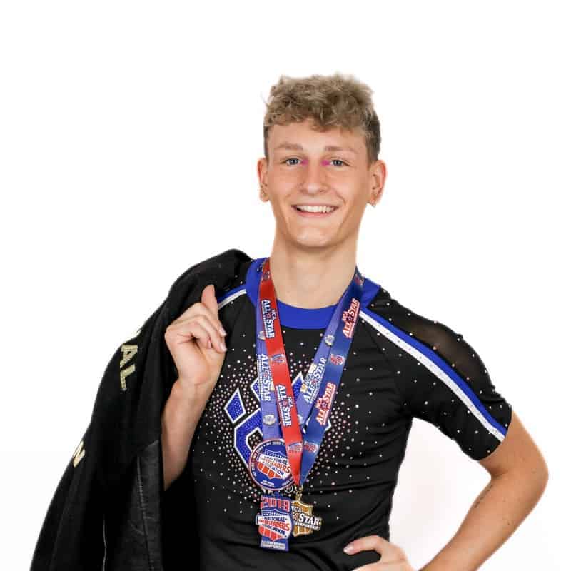 Young male athlete with medals, a championship jacket, and salon-styled hair smiling at the camera.