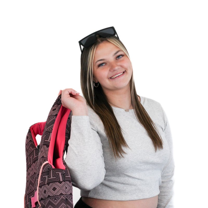 Person smiling, holding a backpack over one shoulder, wearing a gray long-sleeve shirt and sunglasses on head, against a white background.