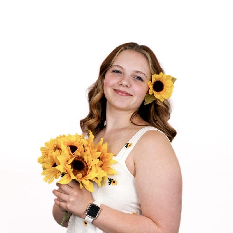 Young woman smiling while holding a bouquet of sunflowers with one flower in her hair, fresh from a beauty salon.