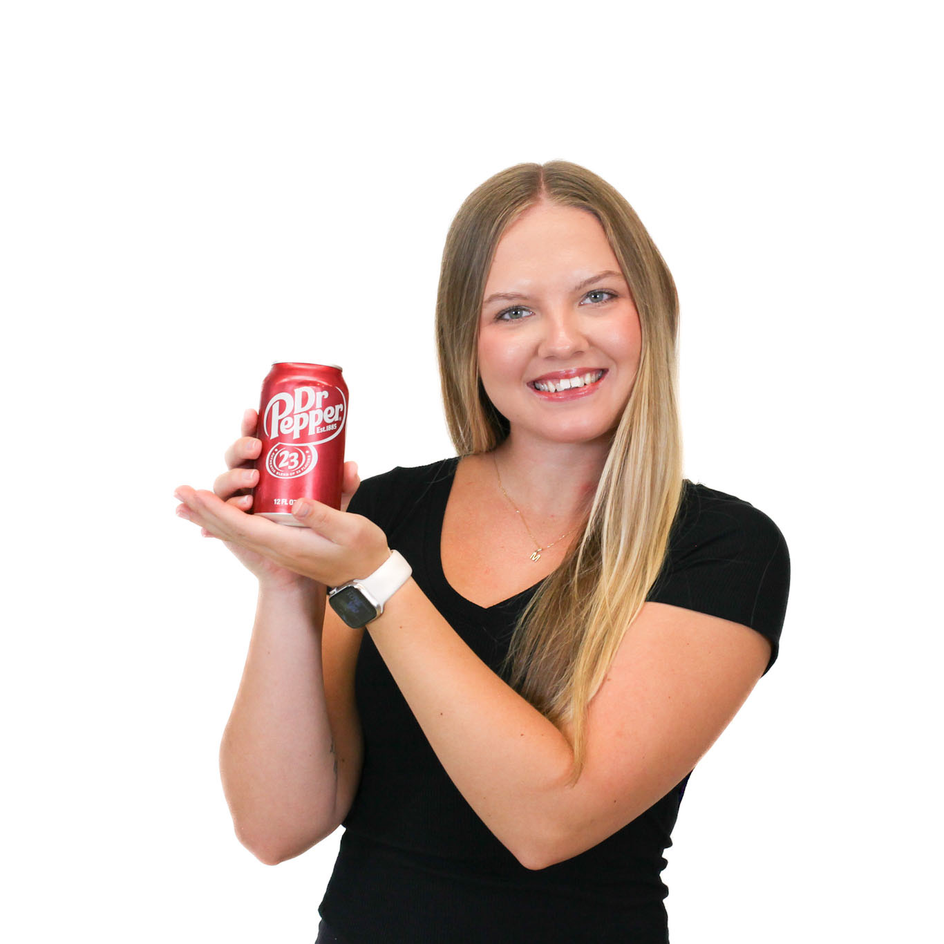 A woman with long blonde hair wearing a black shirt holds and presents a can of Dr Pepper against a plain white background.