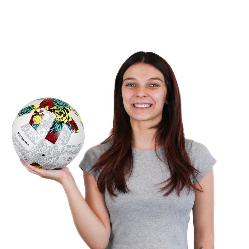 A person with long brown hair smiles while holding a colorful soccer ball against a white background.