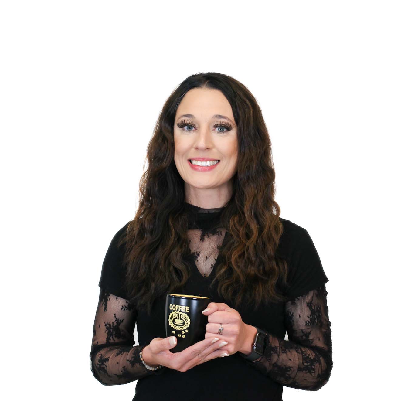 Woman with long brown hair wearing a black lace top, smiling and holding a black coffee mug with "COFFEE" and a cup design printed on it, against a white background.