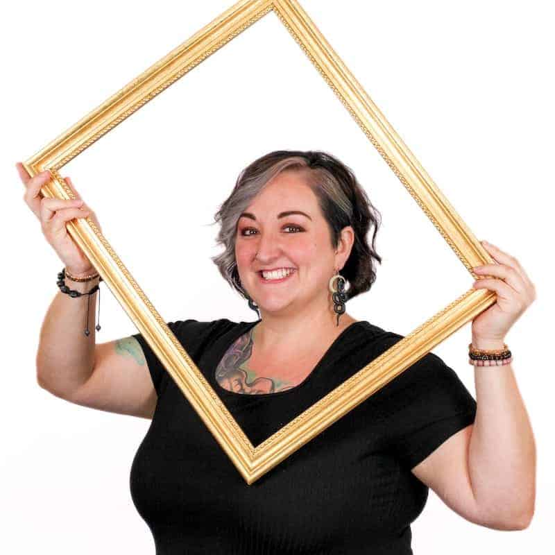 Woman holding a golden picture frame around her face with a cheerful expression, radiating the beauty learned from an Omaha cosmetology school.