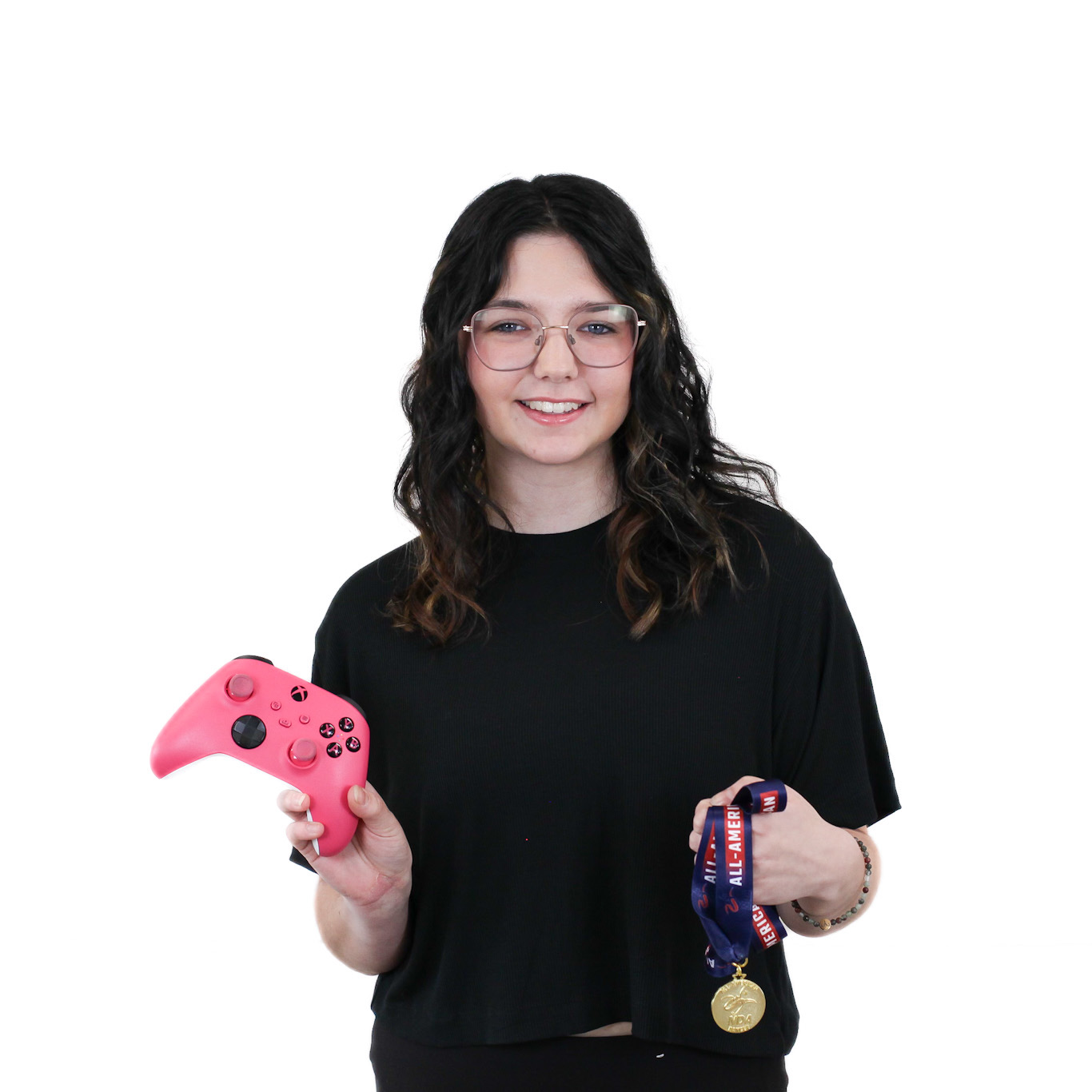 A person with dark hair and glasses holds a pink game controller in one hand and a medal with a "NASEF" lanyard in the other, standing against a white background.