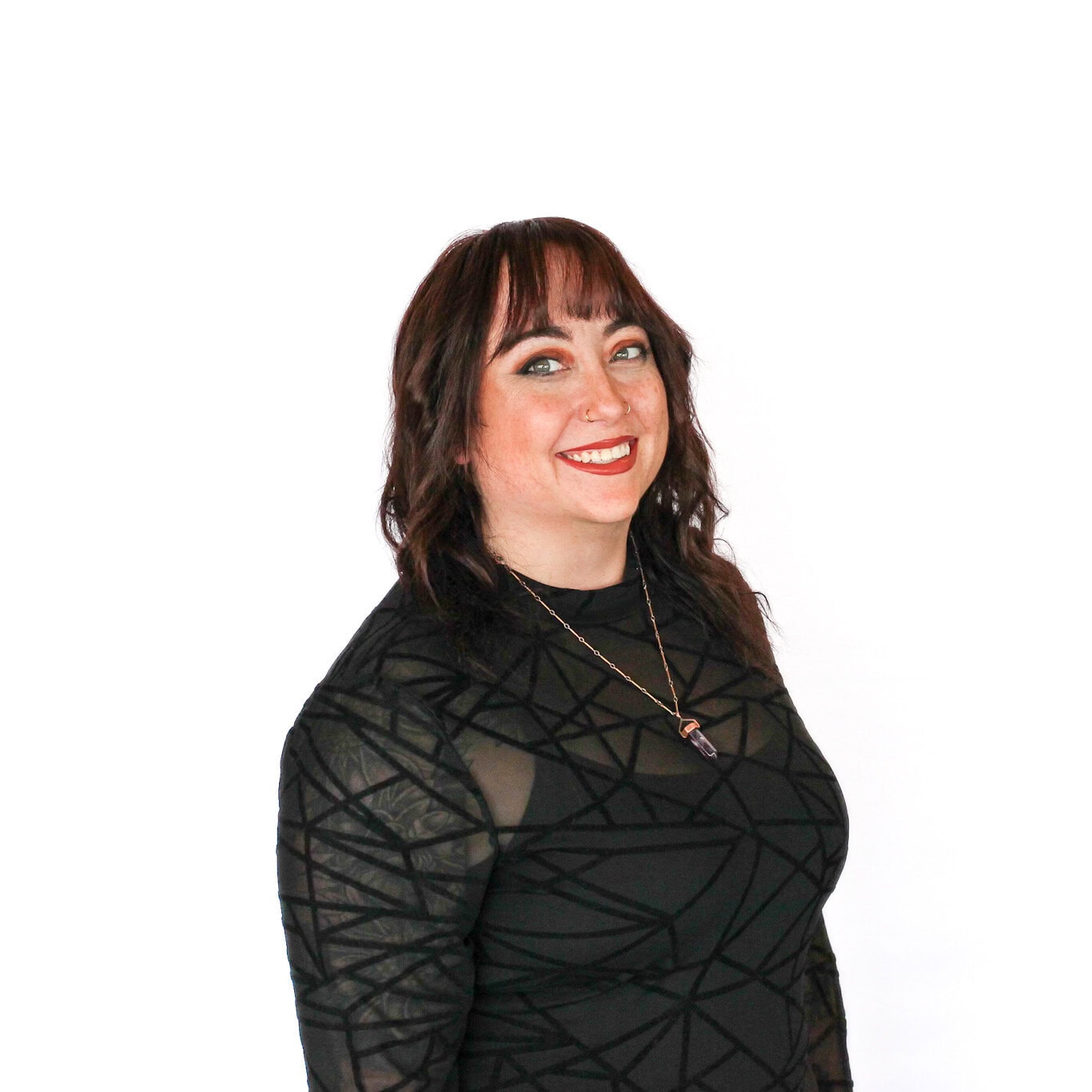 Woman with shoulder-length brown hair, wearing a black geometric-patterned top and a necklace, smiling at the camera against a plain white background.