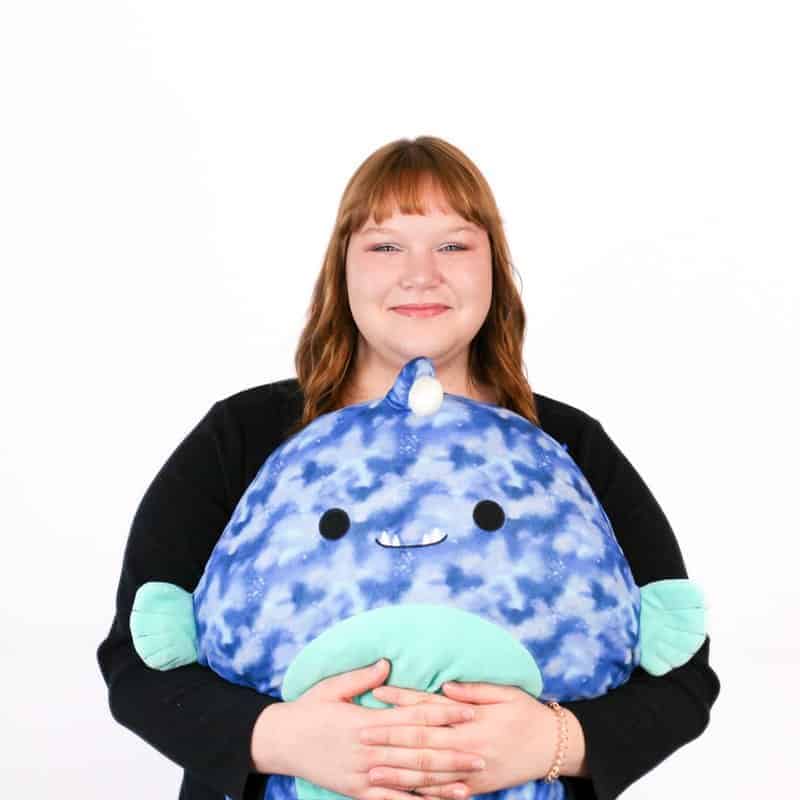 Woman holding a large blue plush toy with a smiling face at an Omaha salon.