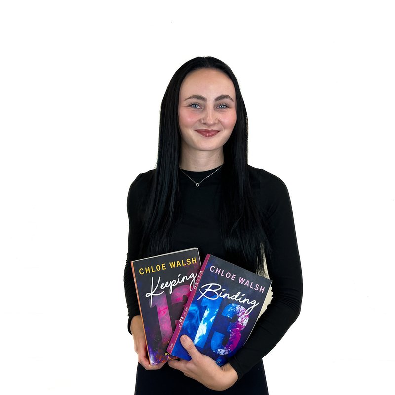 A woman in a black shirt holds two books titled "Keeping" and "Binding" by Chloe Walsh against a white background.