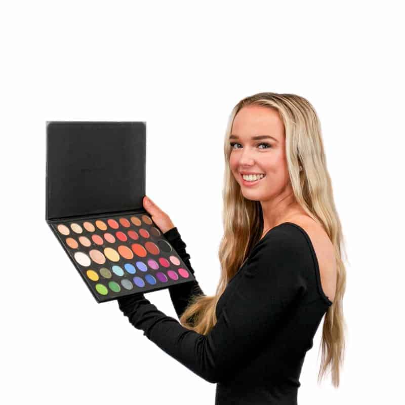 Woman holding a palette of colorful eyeshadows, smiling at the camera, ready for her beauty salon appointment.