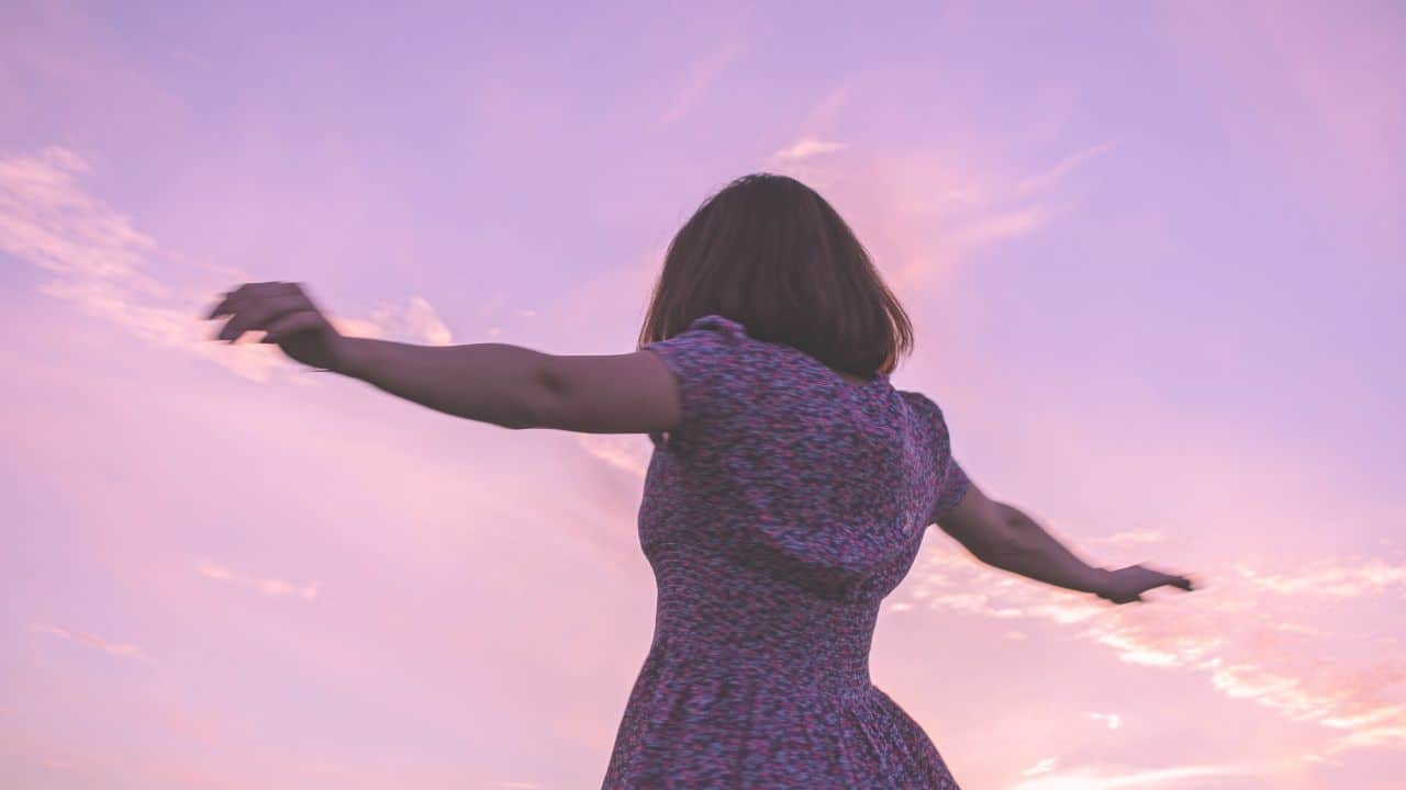A woman with outstretched arms embracing the sunset sky, her hair styled by a renowned Omaha salon.