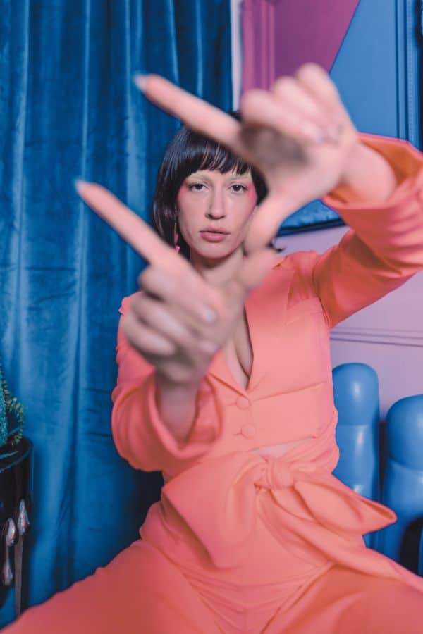 A person in an orange outfit forming frames with their fingers at a hair school.