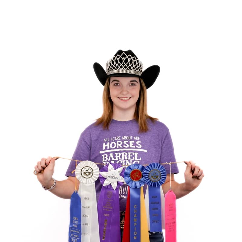 Young female equestrian from Omaha displaying ribbons and wearing a cowboy hat with a tiara.