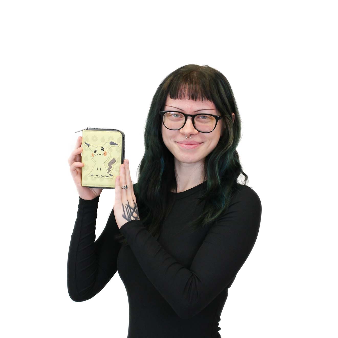 Person with long dark hair and glasses holds up a beige wallet with a Pikachu design, smiling, against a plain white background.