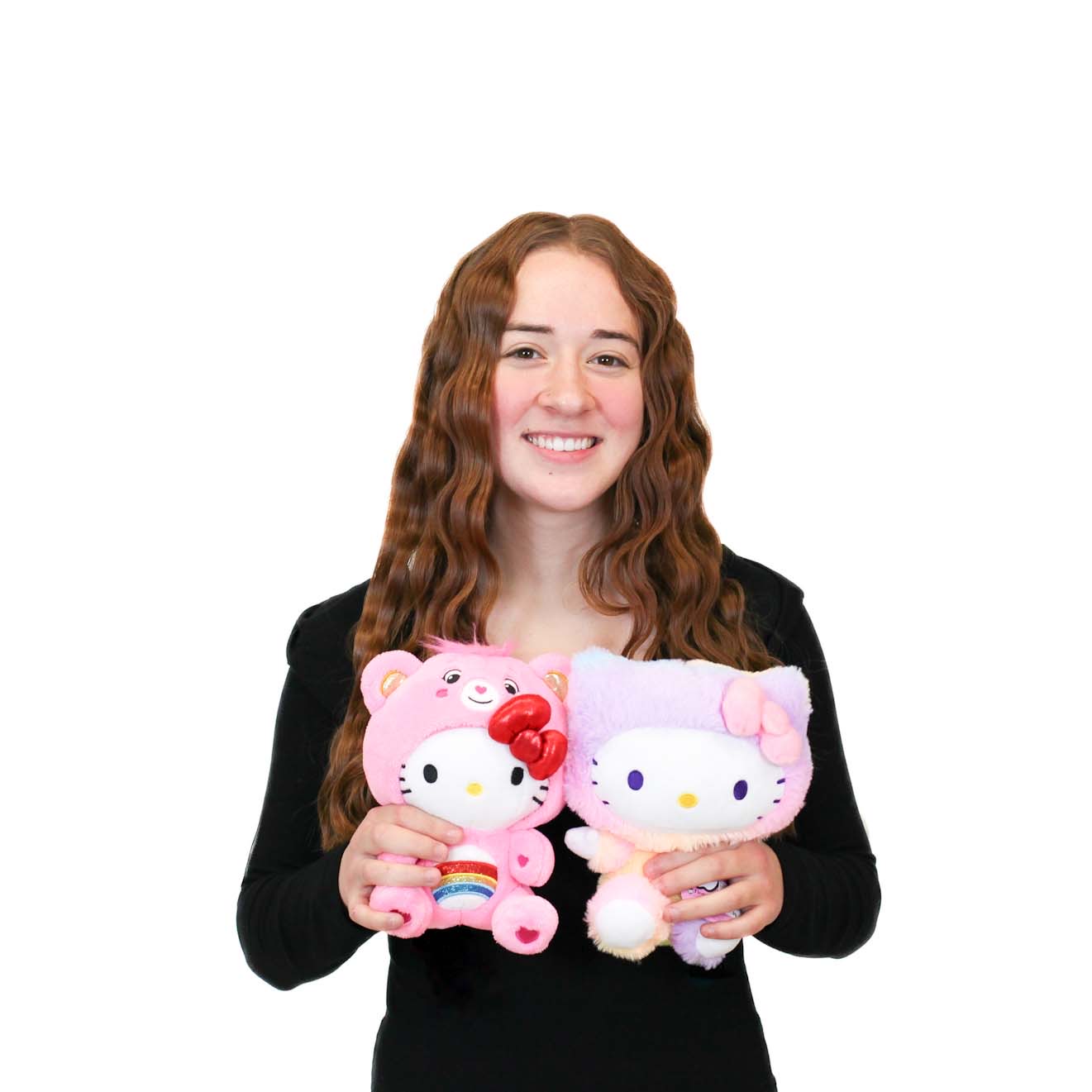 A young woman with long, wavy hair in a black shirt holds two Hello Kitty plush toys, one pink and one lavender, against a plain white background.