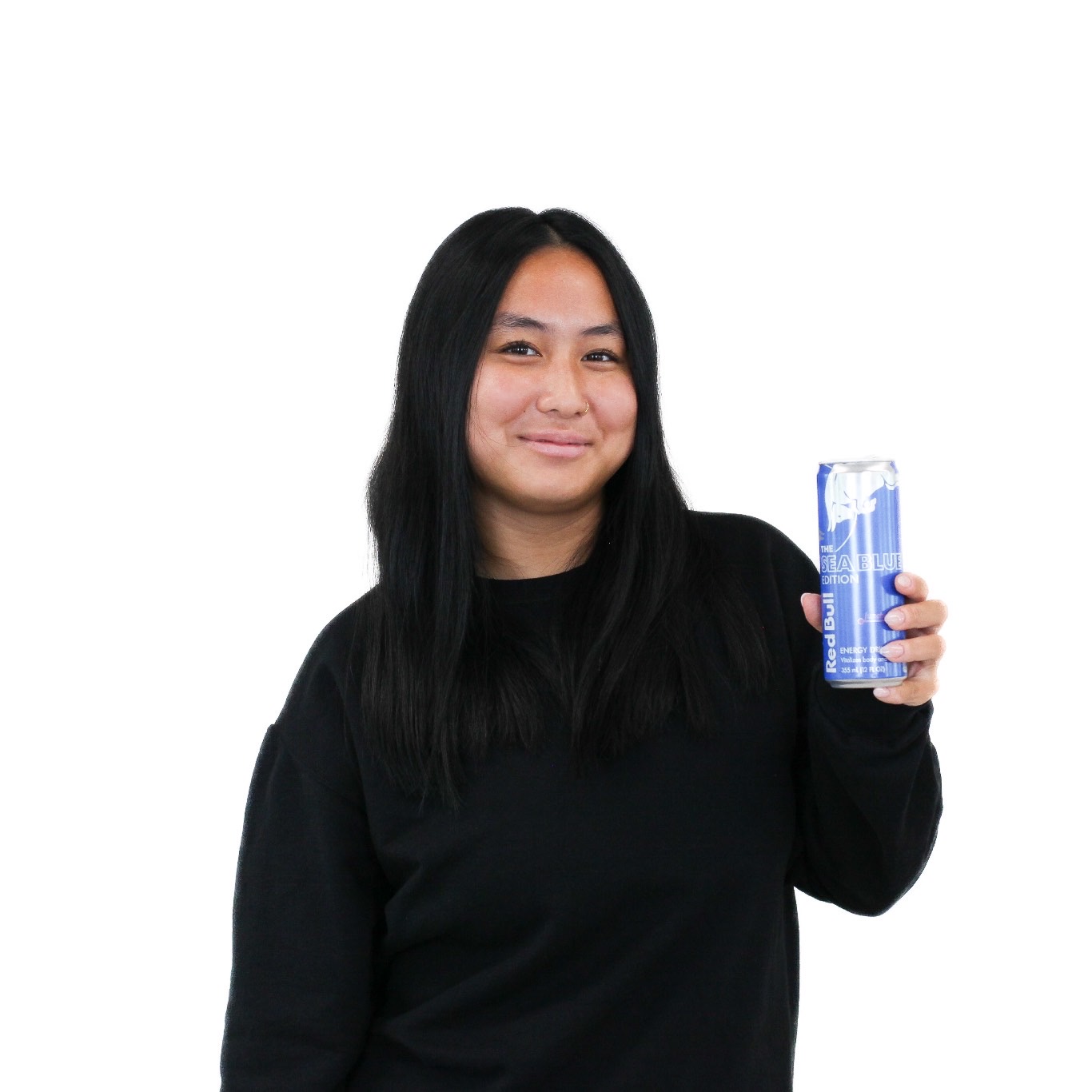 A person with long black hair and a black sweater holds up a blue can, smiling, against a plain white background.