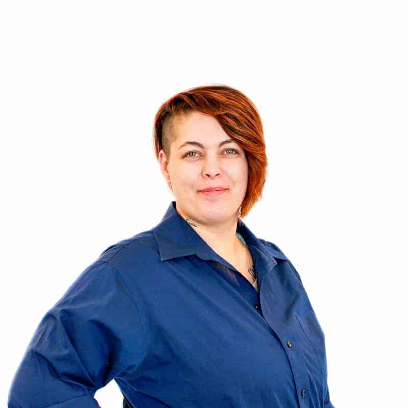 A person with short hair, likely a recent graduate from a cosmetology school in Omaha, wearing a blue shirt stands against a white background.